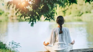 Woman meditating by a peaceful lake in nature.