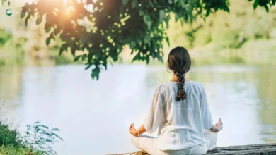 Woman meditating by a peaceful lake in nature.