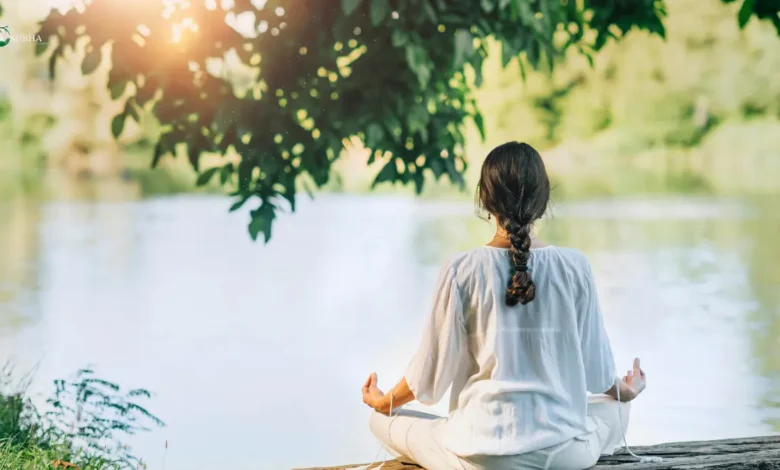 Woman meditating by a peaceful lake in nature.