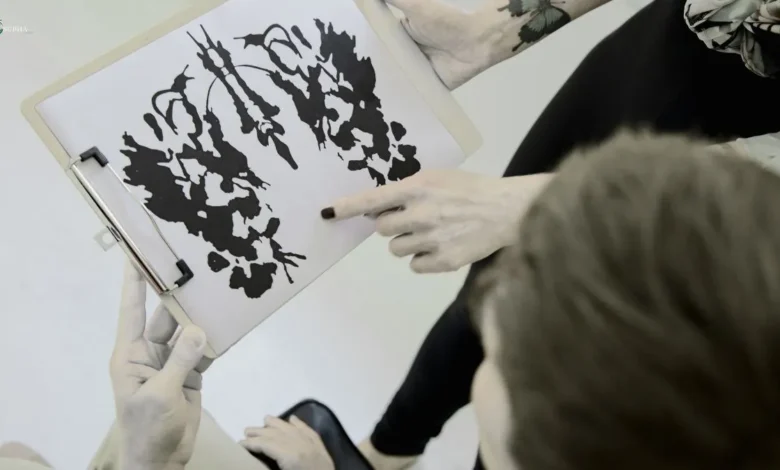 A person pointing at a Rorschach inkblot test on a clipboard while discussing with another individual.