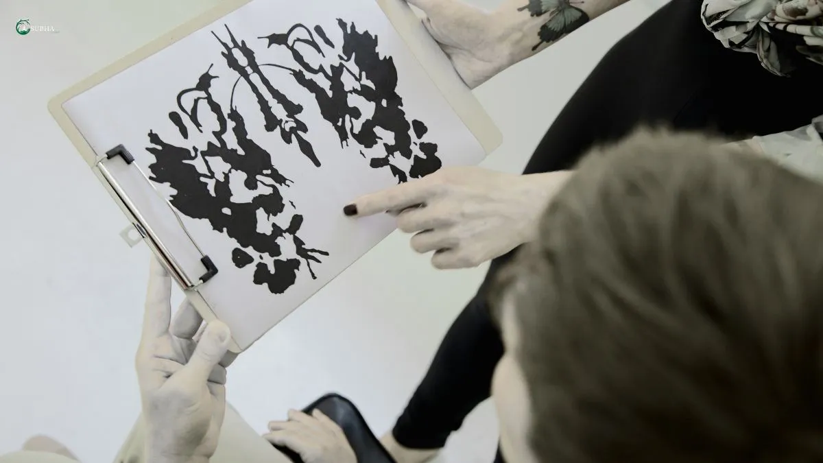 A person pointing at a Rorschach inkblot test on a clipboard while discussing with another individual.