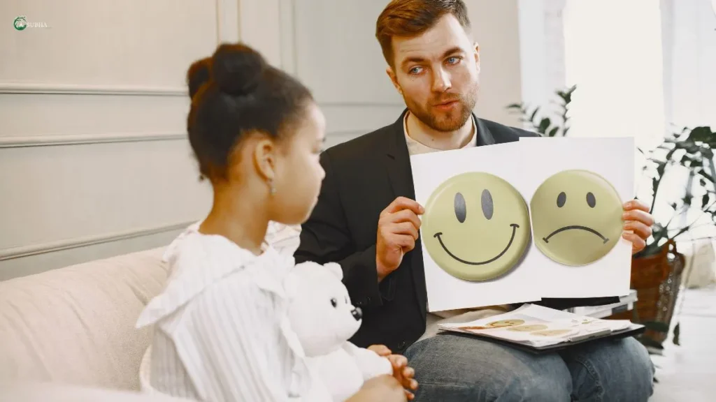 A child in therapy holding a teddy bear while the therapist shows emotion face cards, illustrating emotional expression through visual aids.











